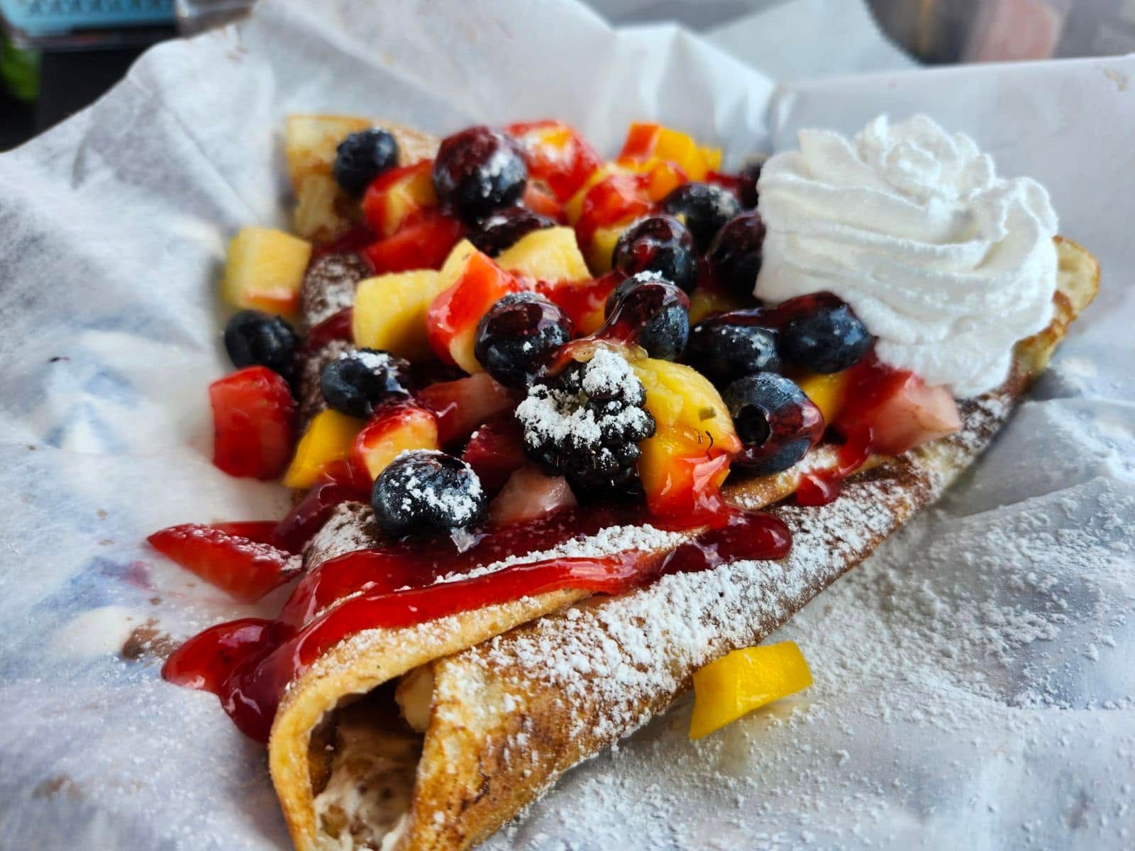 Berry and peach crepe topped with whipped cream and powdered sugar
