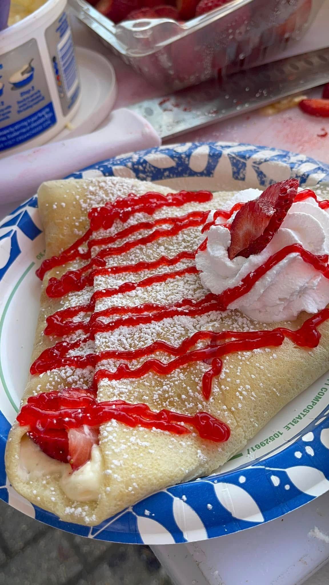 Creamy dessert crepe on a blue-and-white plate, topped with strawberry sauce and whipped cream.