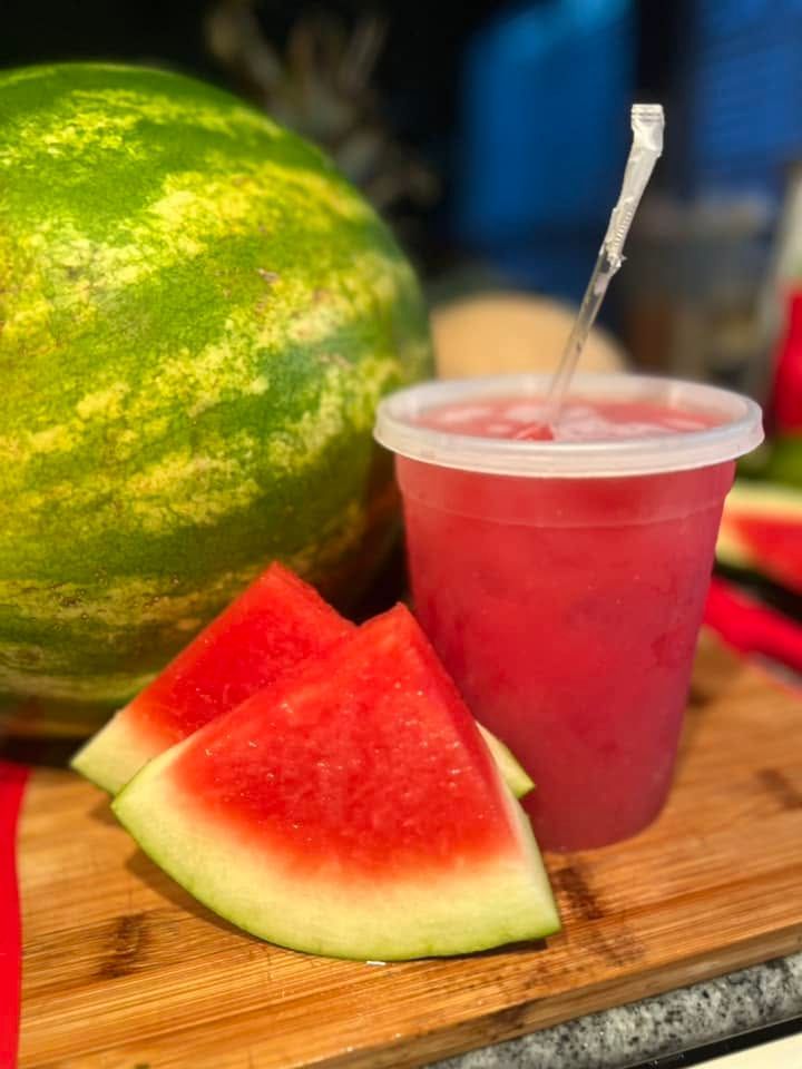 Watermelon slices and a pink drink with a straw beside a whole watermelon on a wooden board.