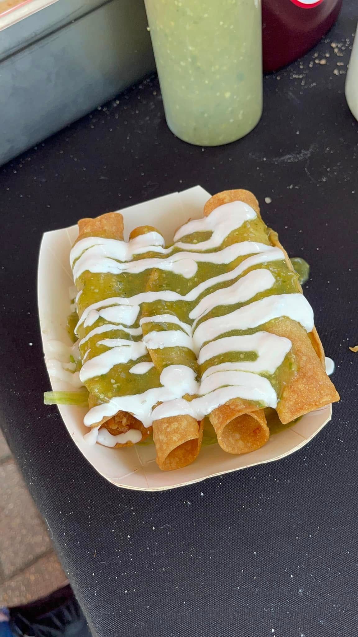 Tray of rolled fried pastries drizzled with white and green sauce on a dark countertop
