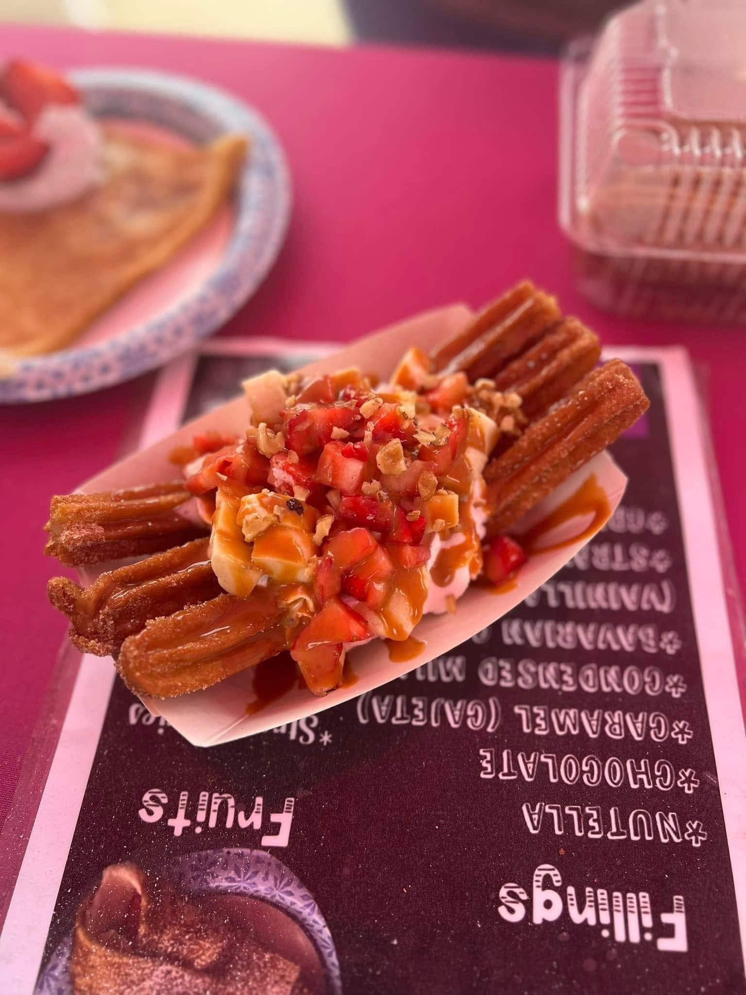 Churro dessert topped with diced fruit on a pink menu card at a cafe table