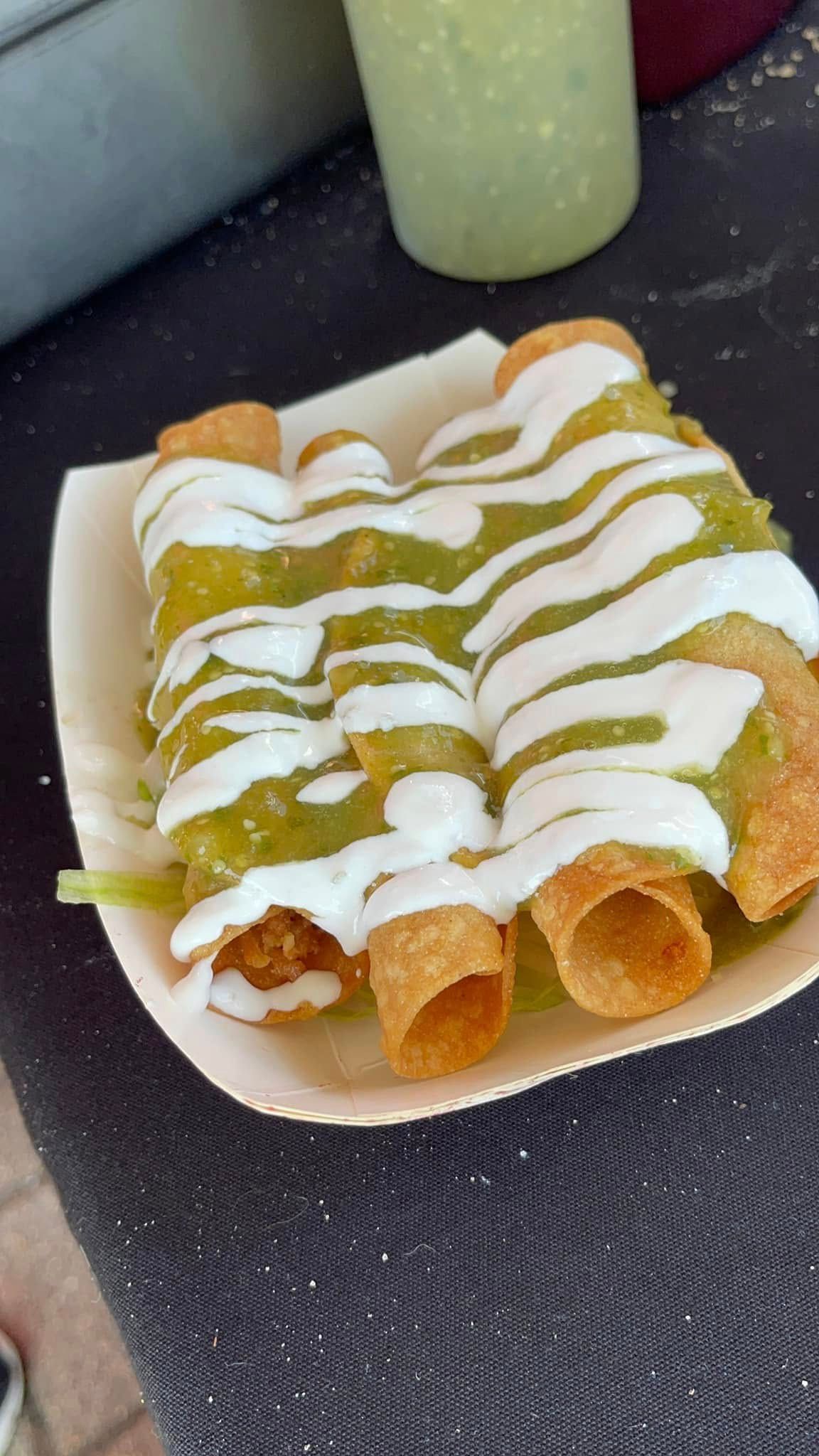 Plate of rolled tacos topped with white and green sauce on a table