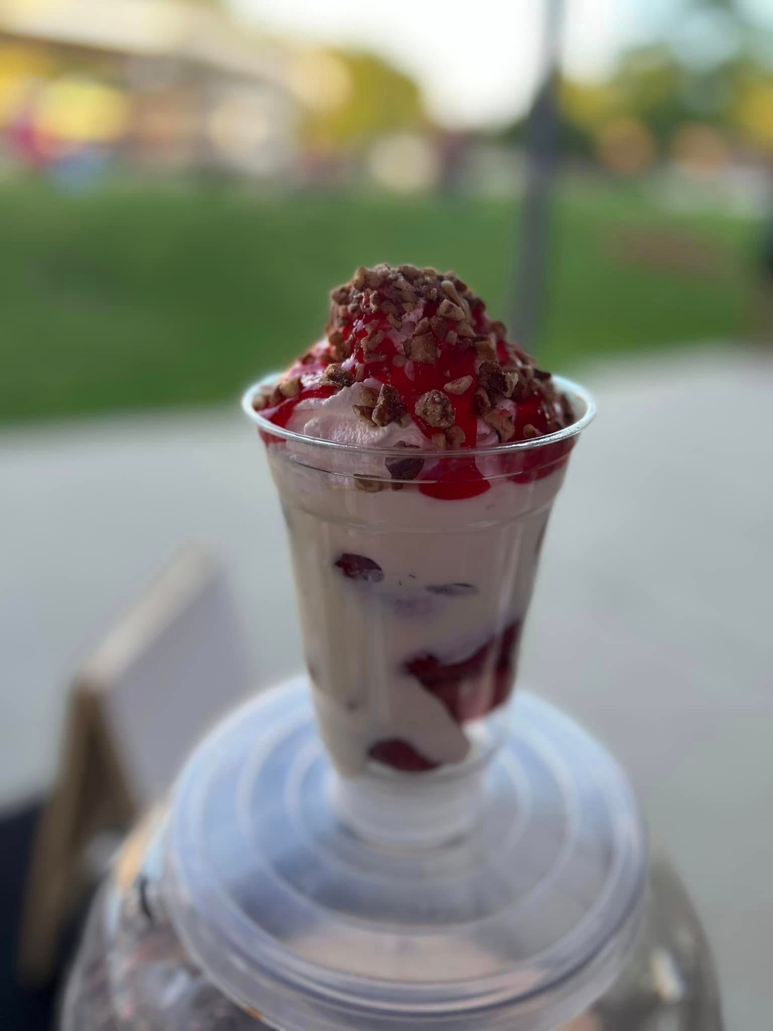 Tall clear cup of white dessert topped with red syrup on a table outdoors
