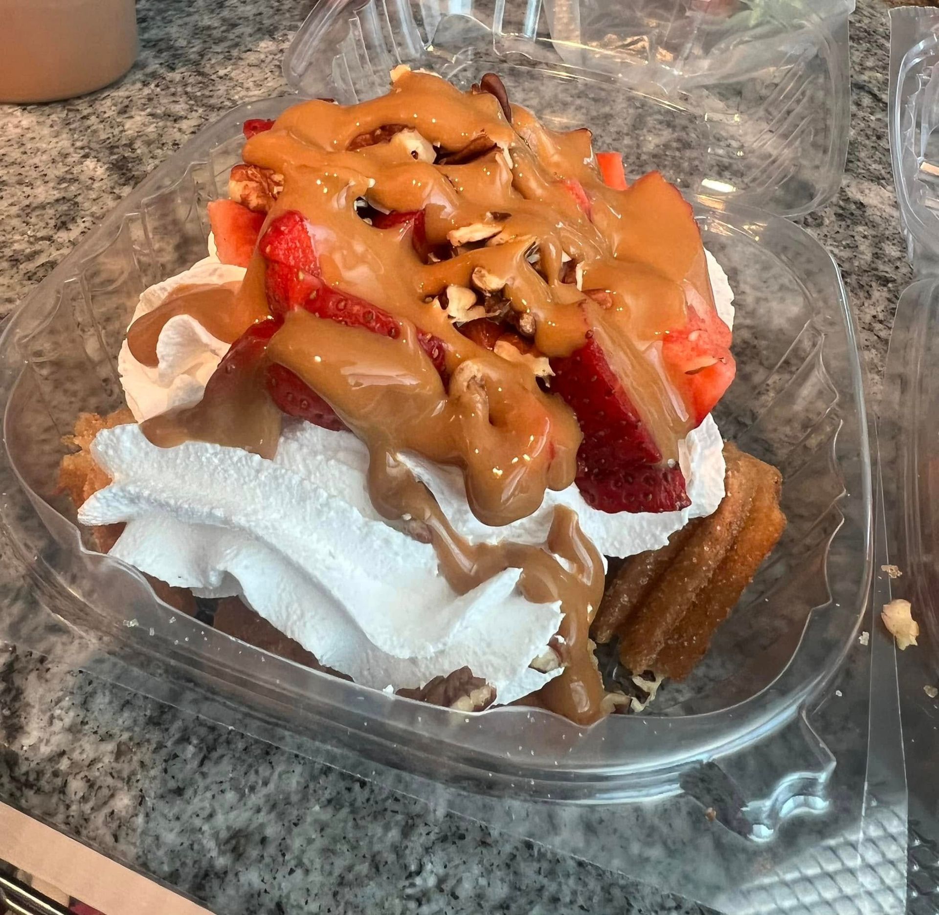 Dessert in a clear plastic container topped with strawberries, whipped cream, and caramel sauce