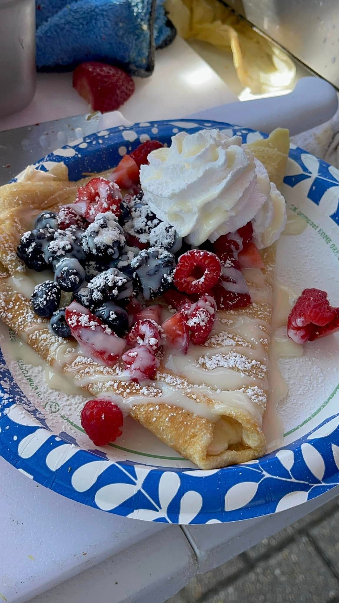 Plate with a crepe topped with whipped cream, powdered sugar, and mixed berries on a table