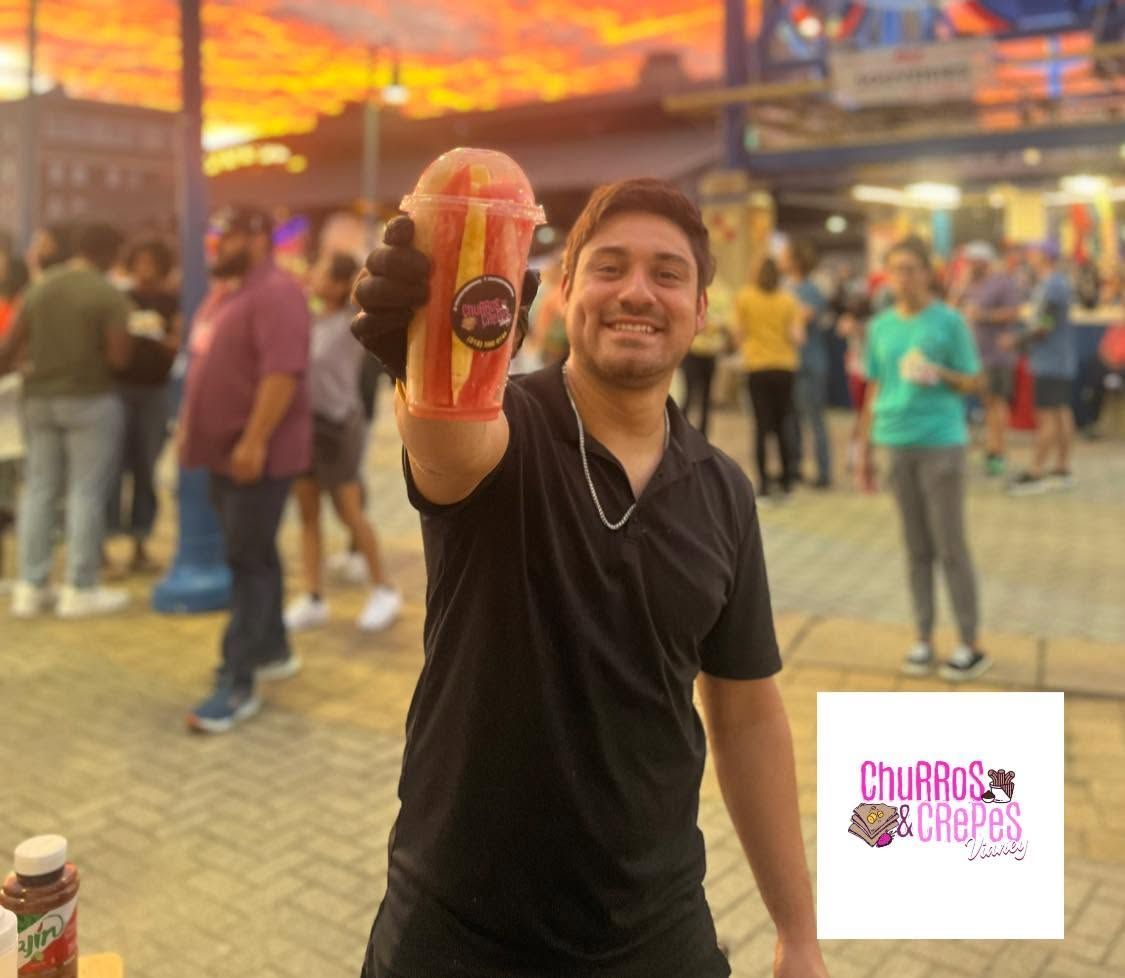 Man holding up a colorful drink at a lively outdoor market at sunset