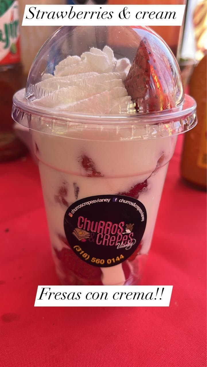 Clear cup of strawberries and cream dessert on a red tablecloth, labeled “Strawberries con crema”