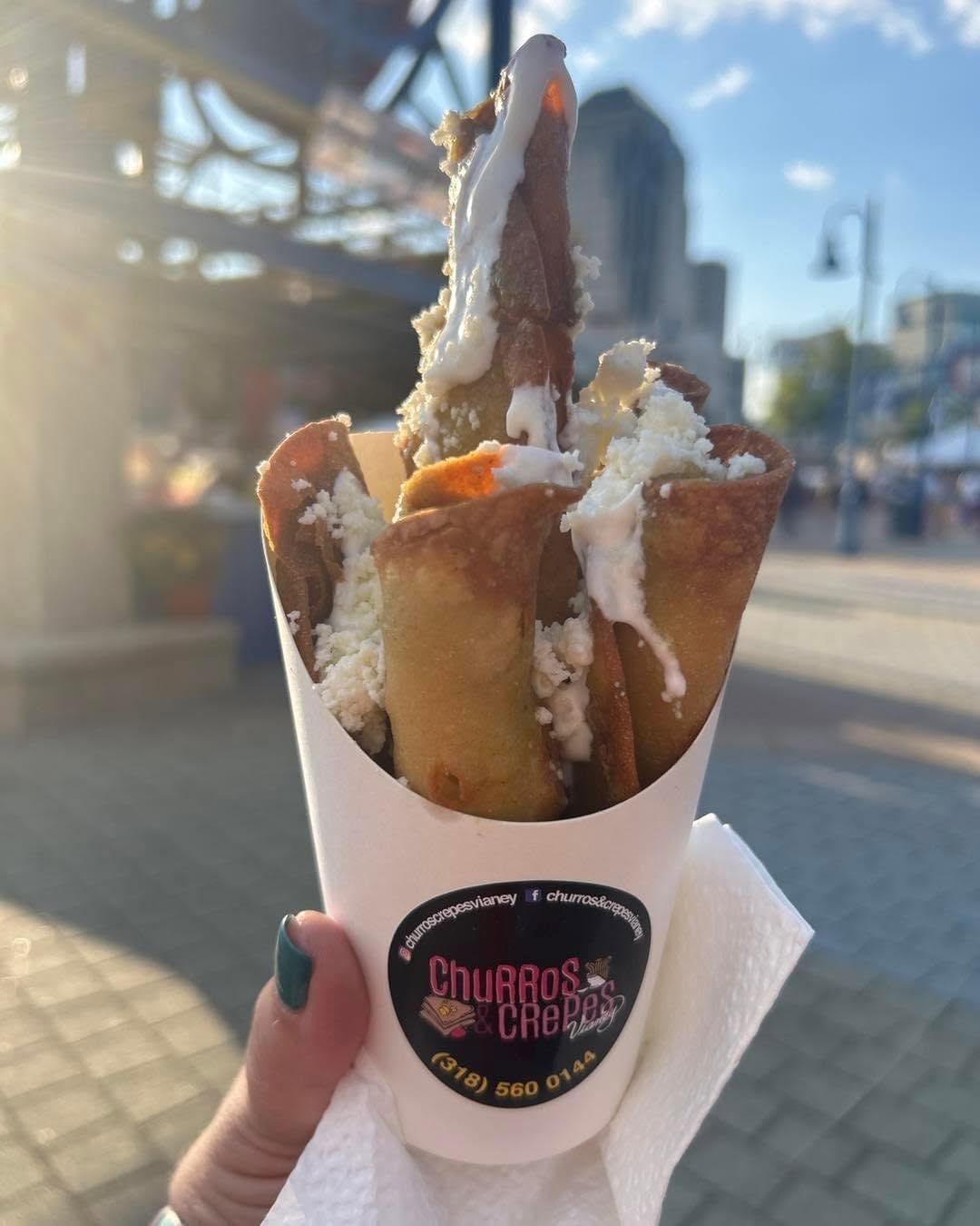 Handheld churro cup topped with whipped cream on a sunny city street, with a Ferris wheel in the background