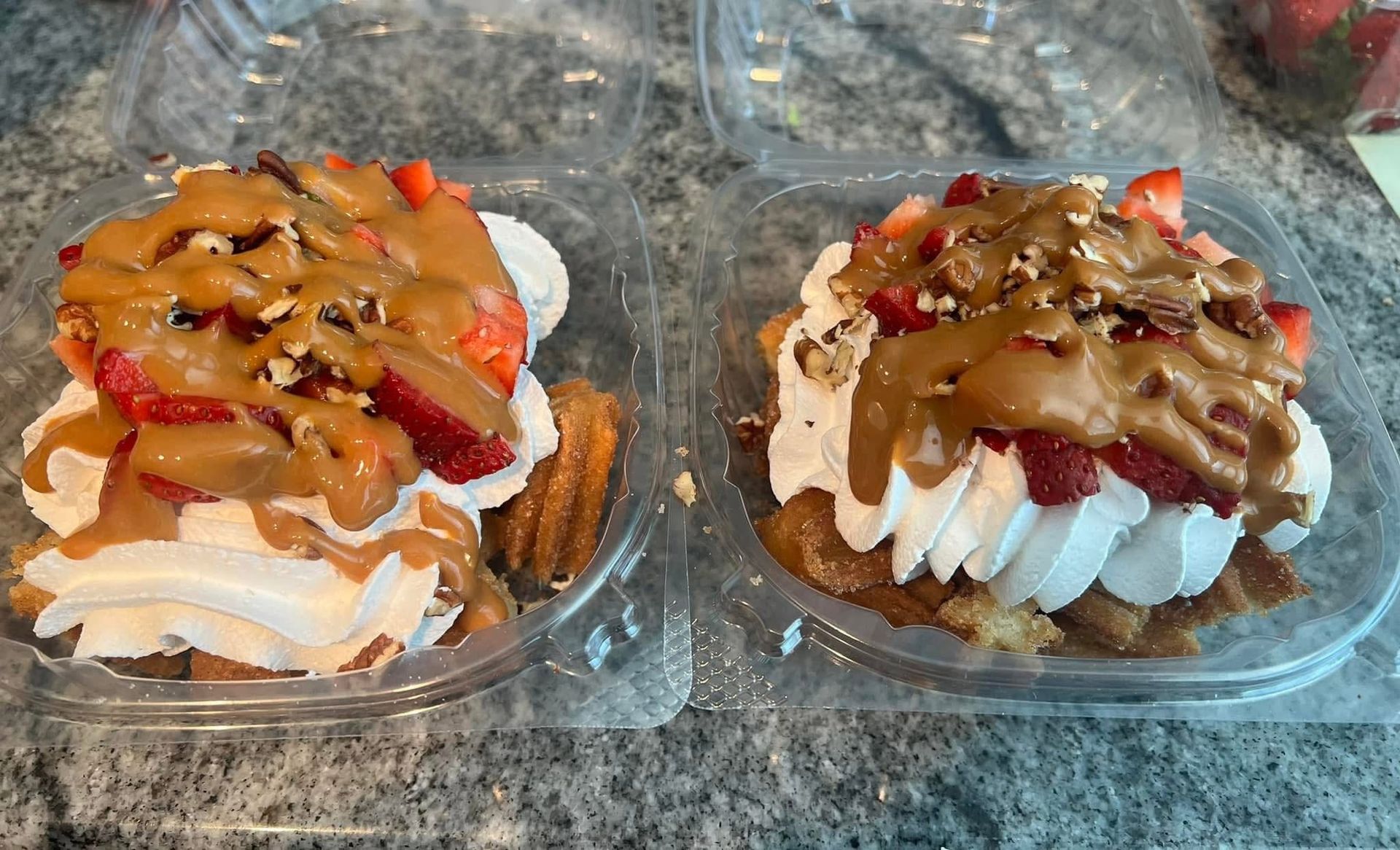 Two dessert pastries in clear plastic containers, topped with caramel, red drizzle, and chopped nuts.