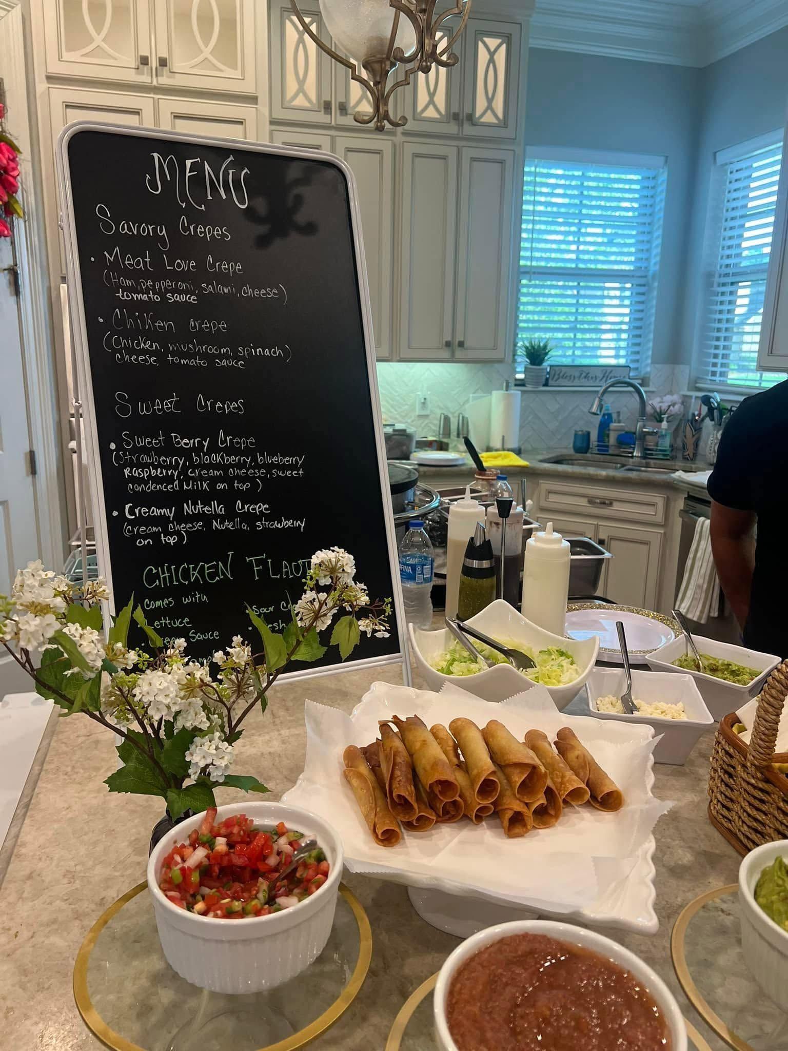 Buffet table with tacos, salsa, flowers, and a chalkboard menu in a bright kitchen