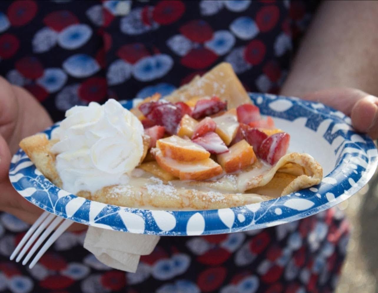 Plate of strawberry peach dessert pie with whipped cream, held by hands on a patterned blue paper plate