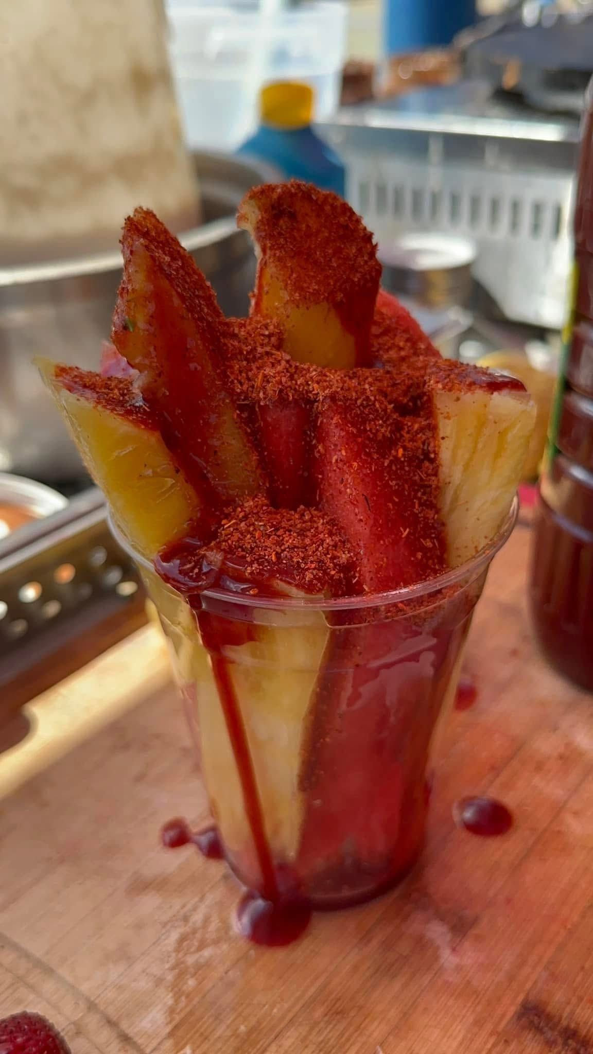 Red berries in a clear cup on a wooden table, with red syrup dripped inside.