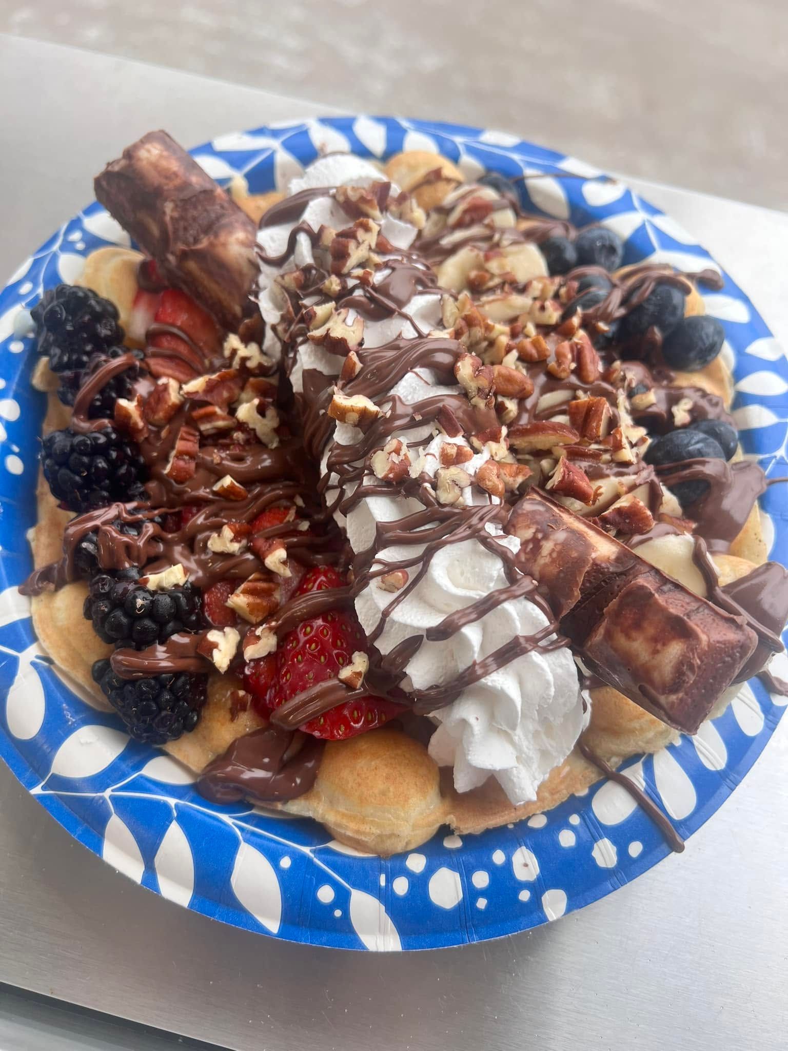 Blue plate with chocolate-drizzled crepes topped with whipped cream, berries, and nuts