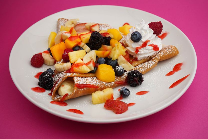 Pastry plate topped with berries, diced fruit, whipped cream, and chocolate drizzles on a pink background