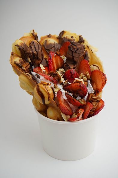 White cup filled with waffle fries topped with strawberries, chocolate drizzle, and powdered sugar