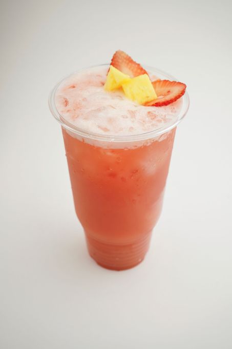 Pink peach smoothie in a clear plastic cup topped with peach slices and foam against a white background