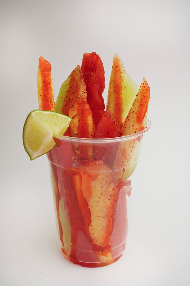 Cup of chili-dusted fruit sticks with a lime wedge on a white background