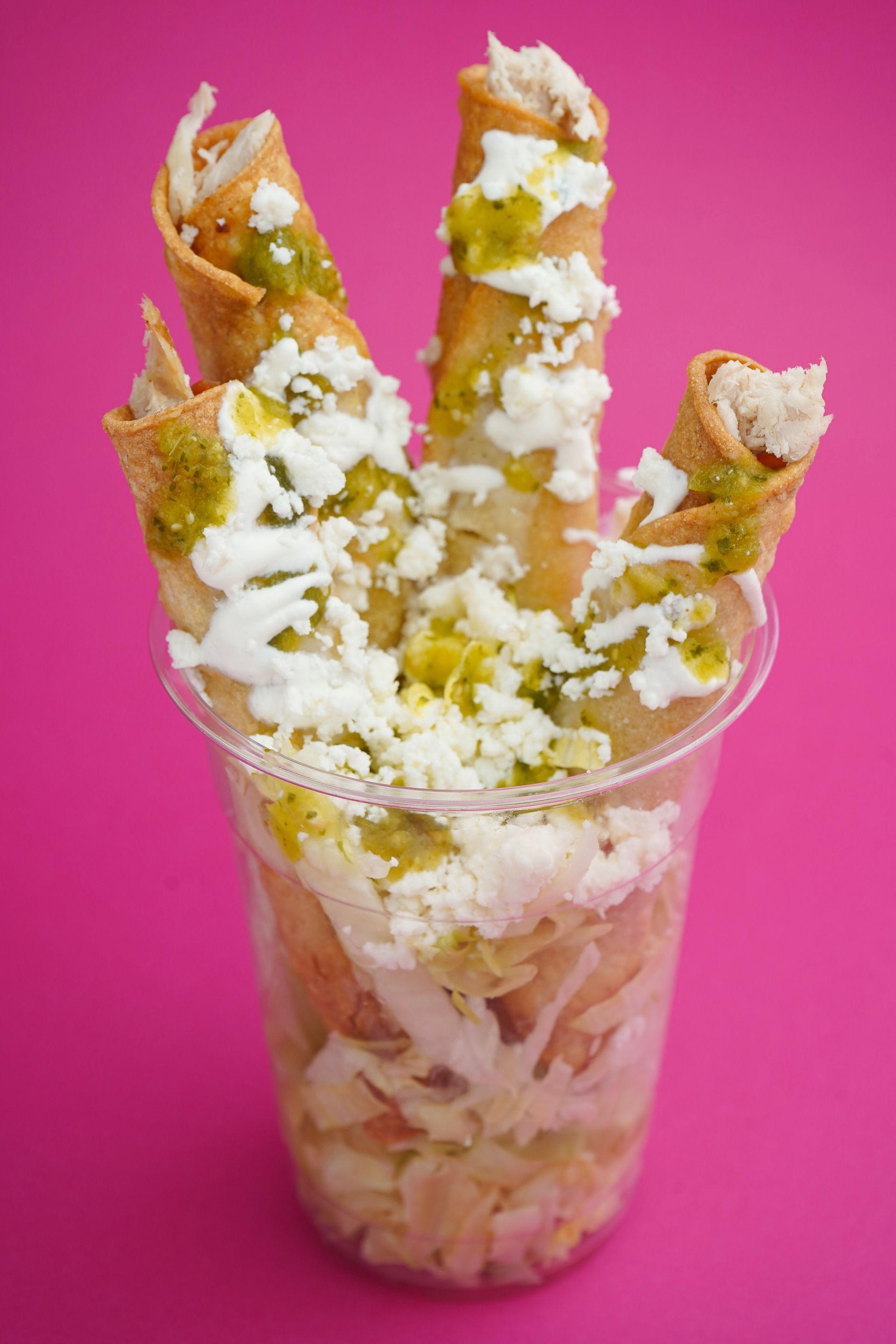 Dessert cup with rolled waffles topped with whipped cream and powdered sugar on a pink background