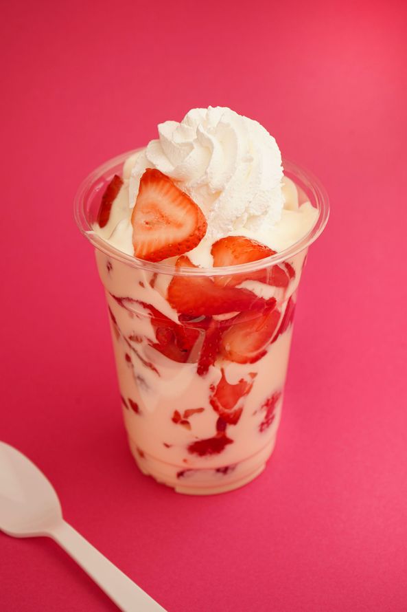 Strawberry parfait topped with whipped cream in a clear cup on a bright pink background