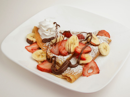 Waffle topped with strawberries, bananas, whipped cream, and chocolate drizzle on a white plate