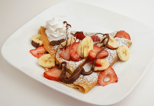 Dessert crepe topped with strawberries, bananas, whipped cream, and chocolate sauce on a white plate