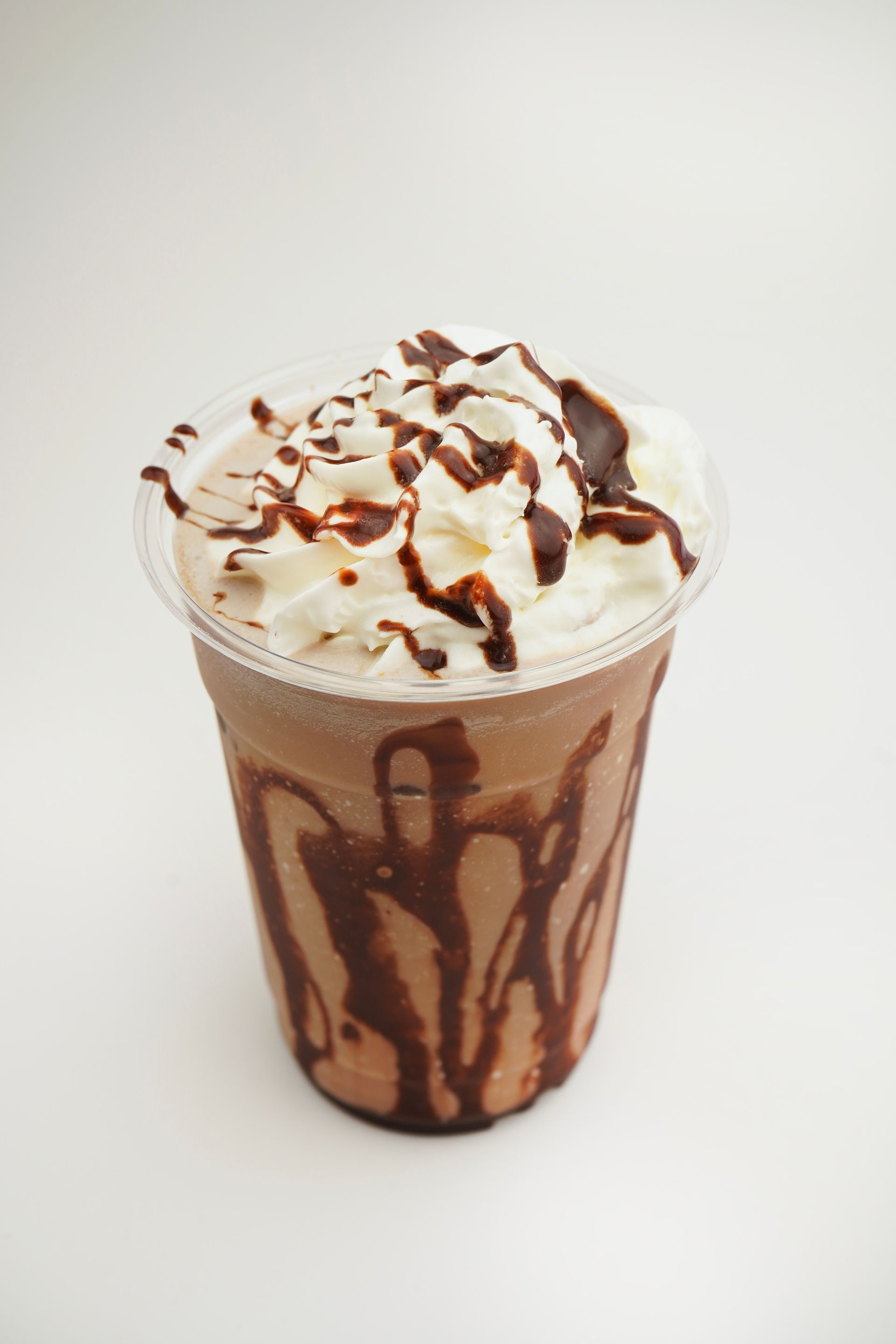 Chocolate-drizzled whipped cream milkshake in a clear cup on a plain white background