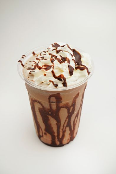 Chocolate-drizzled whipped cream milkshake in a clear cup on a plain white background