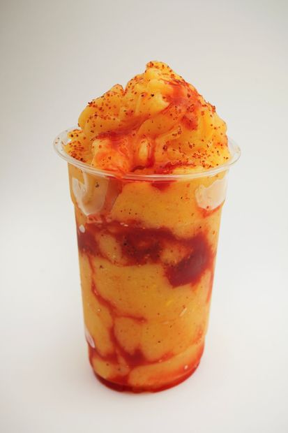 Clear cup of mango dessert with red syrup drizzles and shaved ice on top