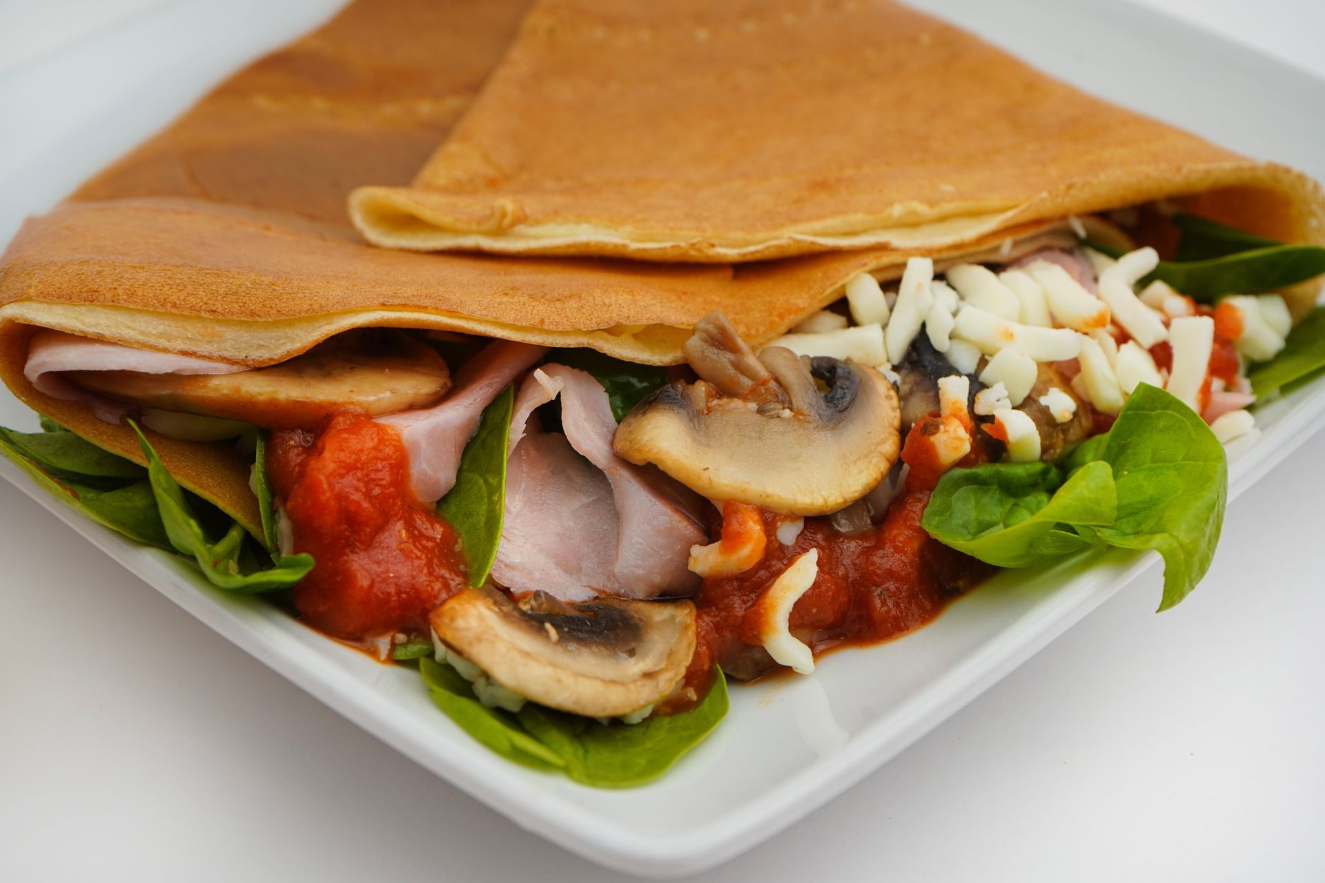 Folded crepes with mushrooms, tomato sauce, greens, and cheese on a white plate