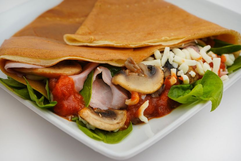 Folded crepes with mushrooms, tomato sauce, greens, and cheese on a white plate