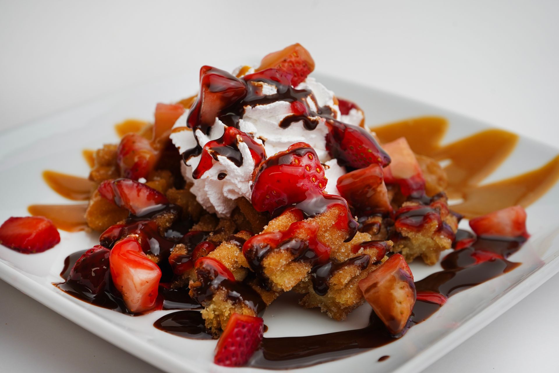 Dessert plate with waffles topped with strawberries, whipped cream, chocolate, and caramel sauce