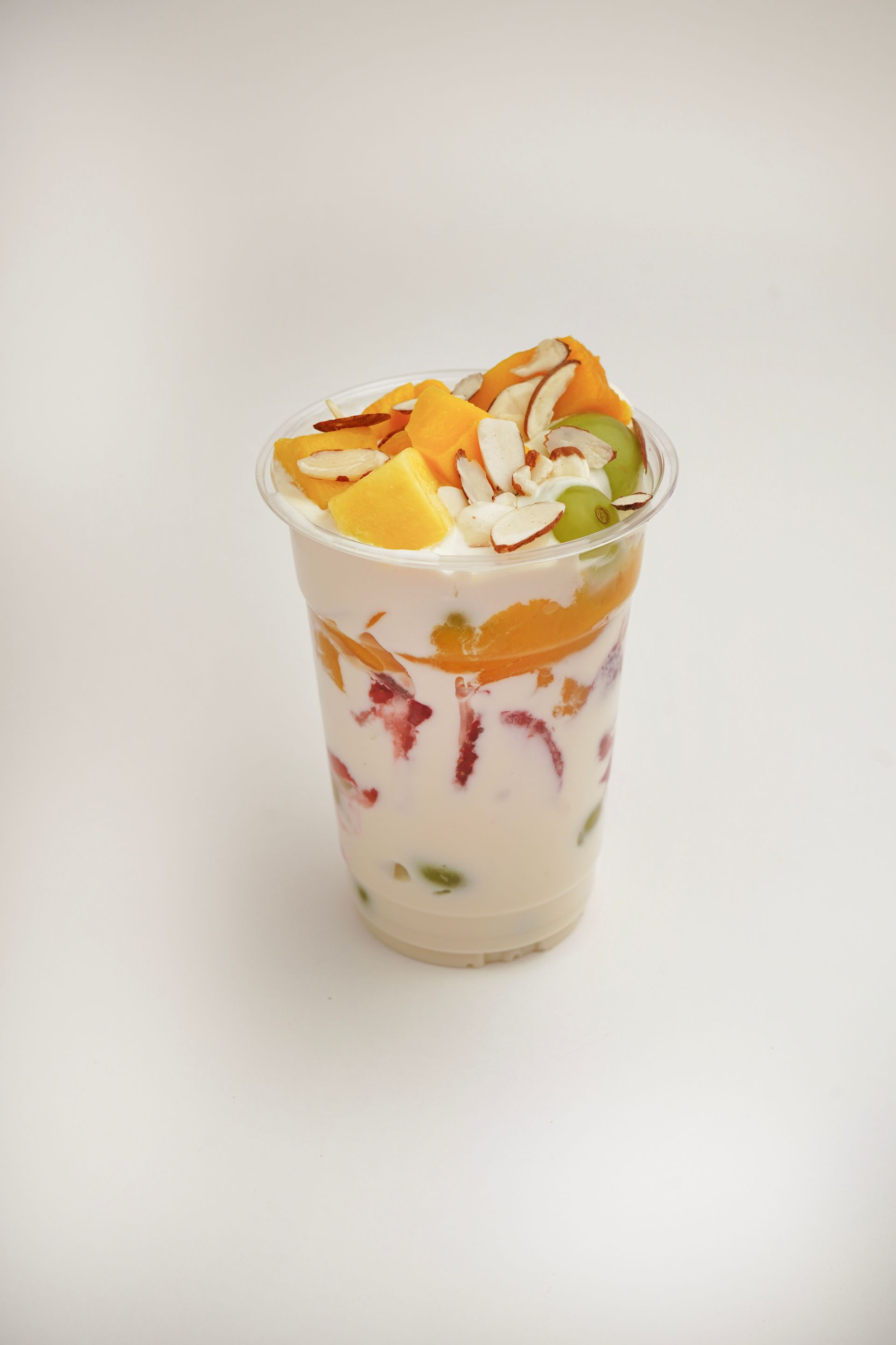 Colorful layered dessert in a clear cup with fruit and whipped cream on a white background