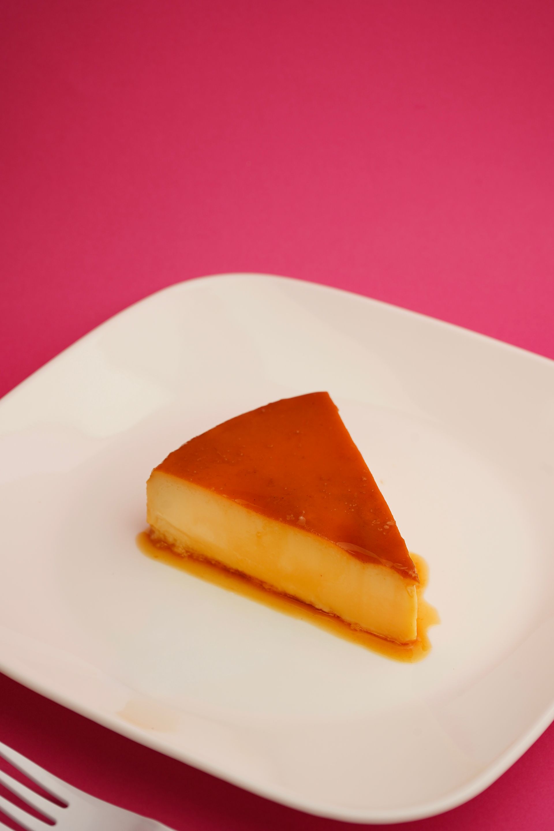 Slice of flan on a white plate against a pink background