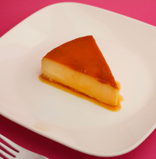 Slice of caramel flan on a white plate with a fork, on a pink background
