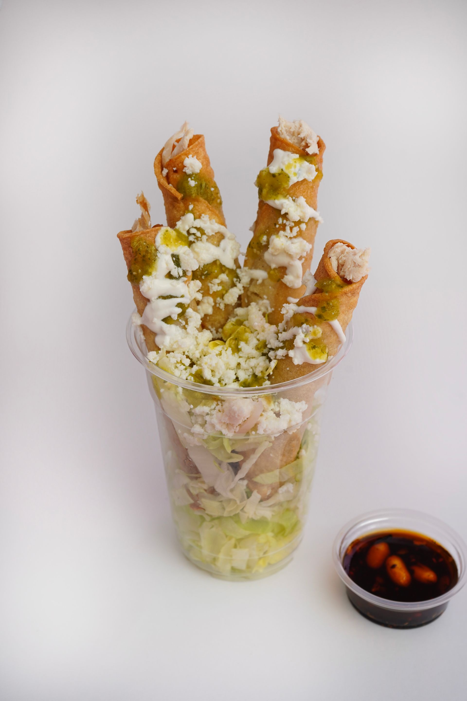 Tall cup of cheese-covered fried sticks with a side of dipping sauce on a plain background
