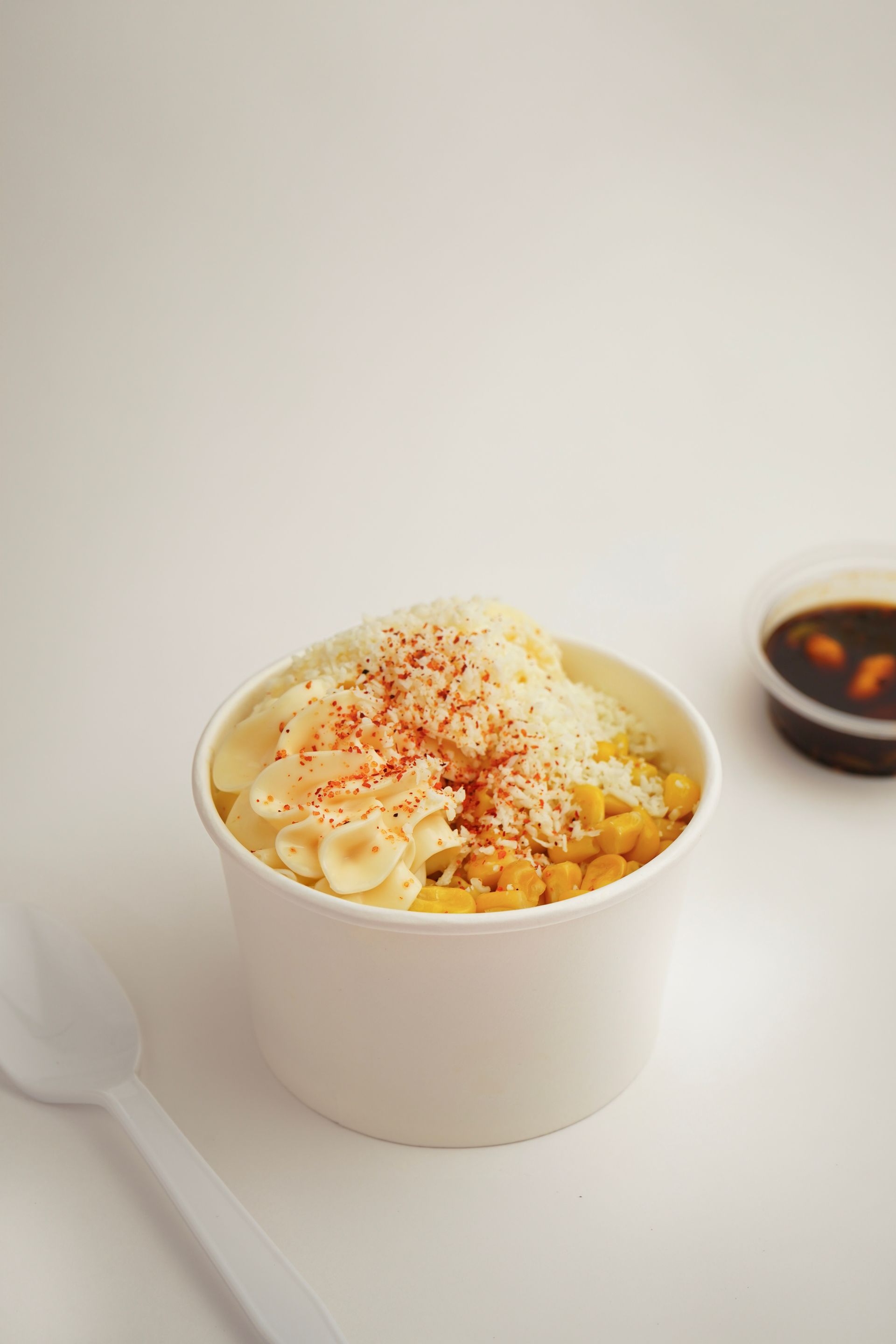 Cup of macaroni and cheese topped with seasoning on a white table, with a spoon beside it.
