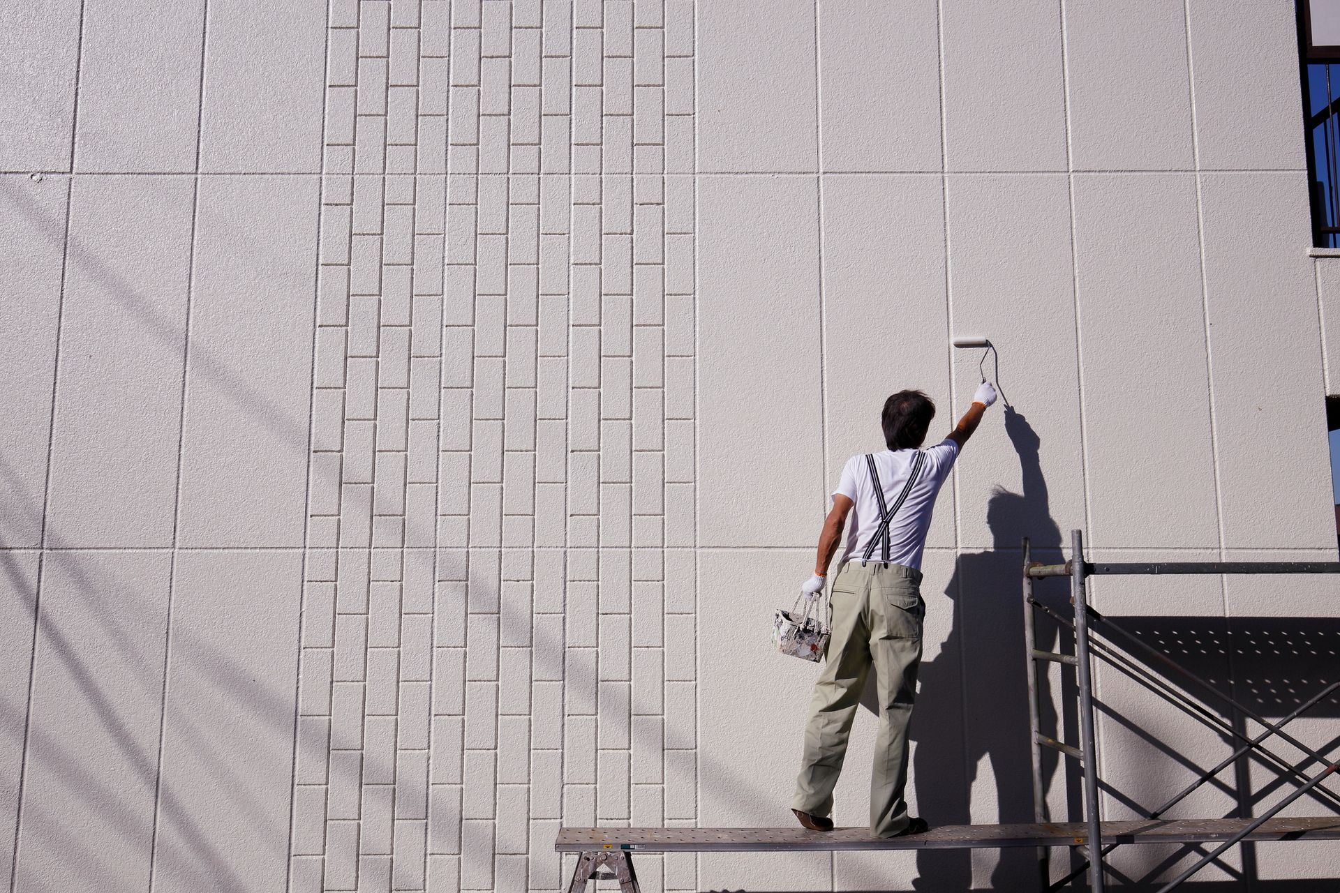 Business painting worker safely painting the high exterior wall of a commercial building.