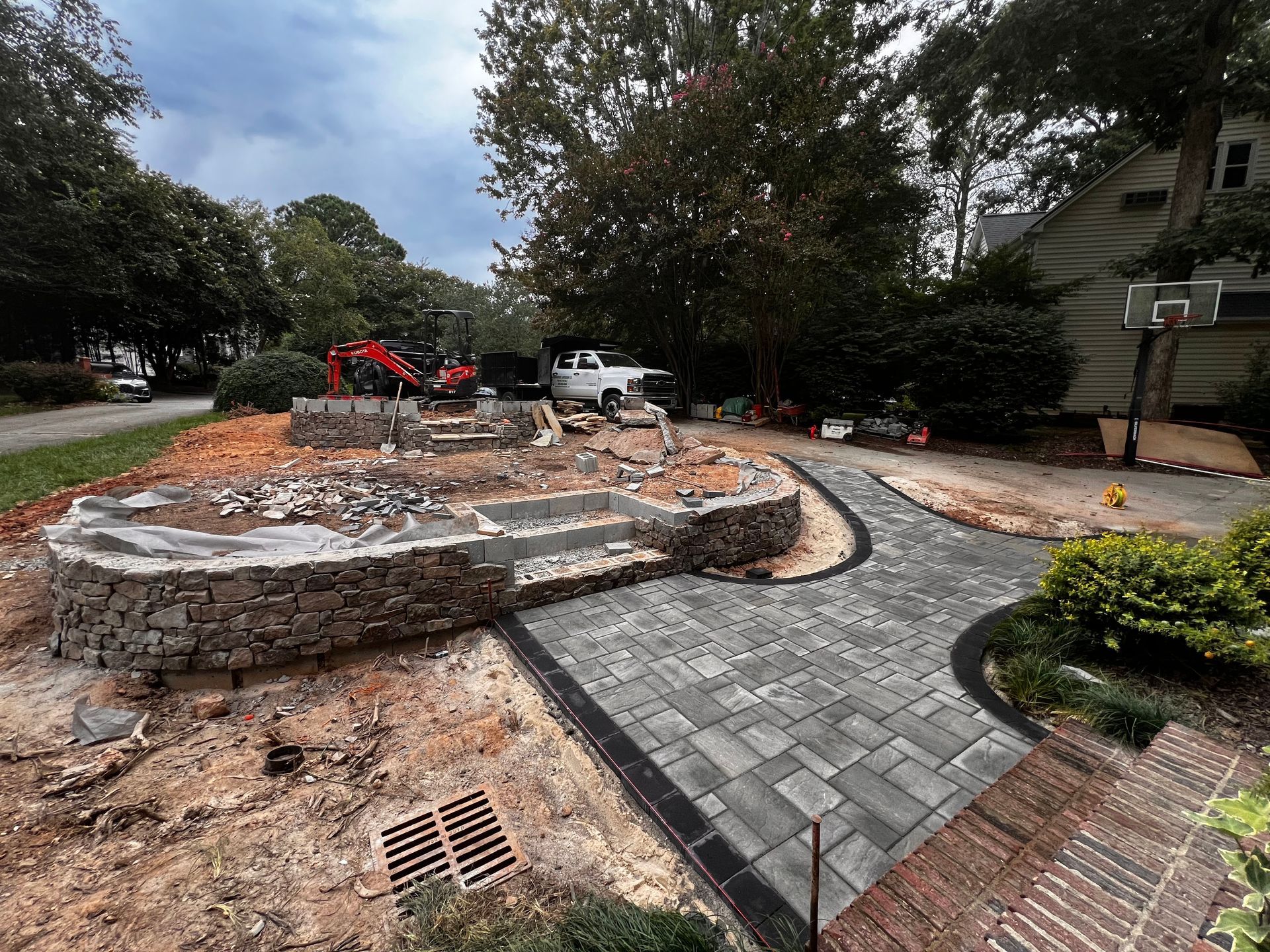 Stone patio with winding paver path, stacked rock seating, and a small construction vehicle in a landscaped yard