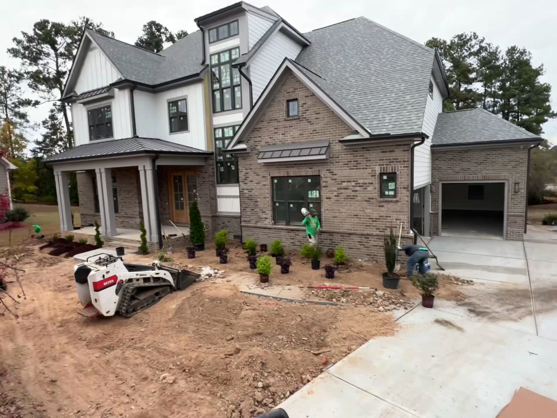 Newly built two-story house with stone and white siding, front porch, driveway, and landscaping underway