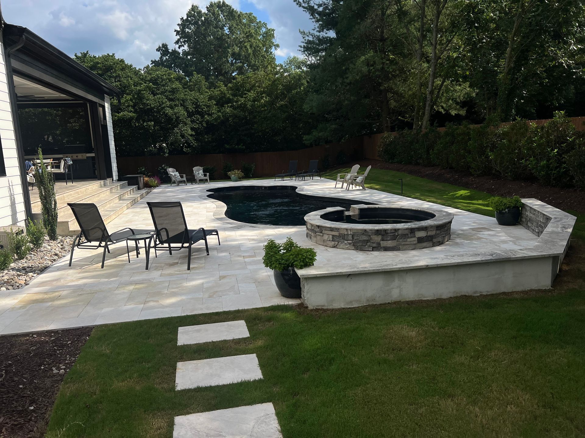 Backyard patio with circular fire pit, lounge chairs, and stepping stones leading across the lawn