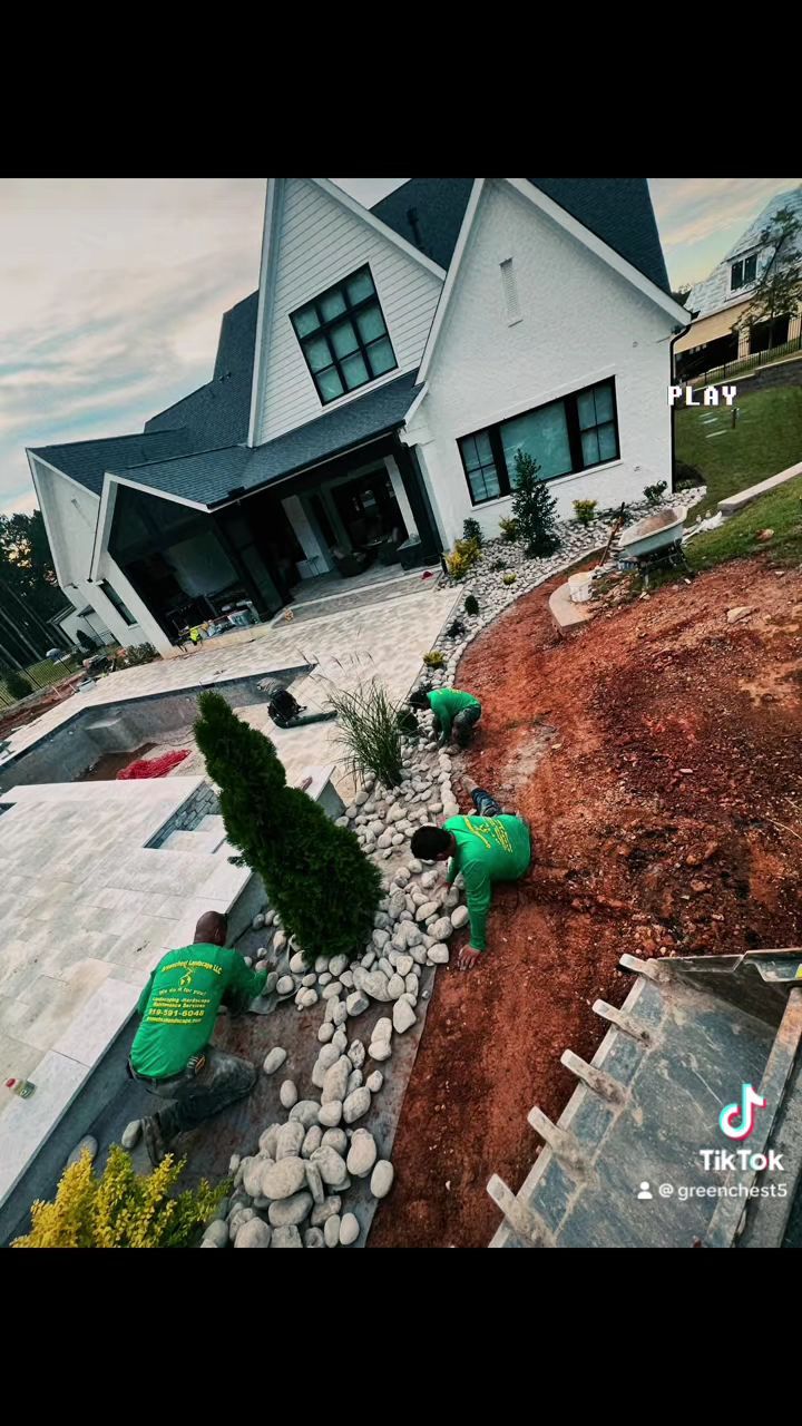 Tilted view of a white house with a stone walkway, small trees, and green landscaping bags in front