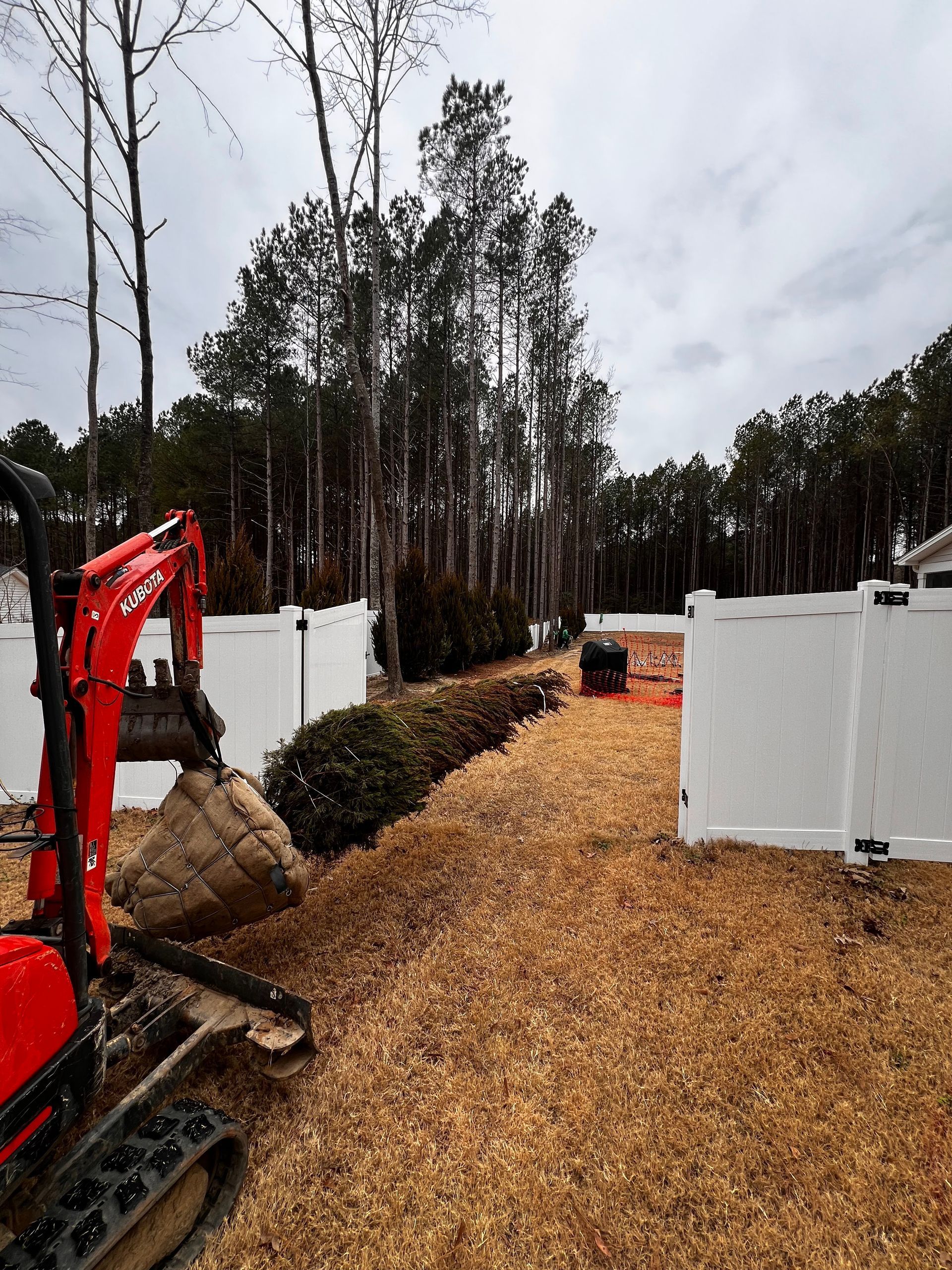 Red excavator beside a woodchip path between white fences in a wooded area