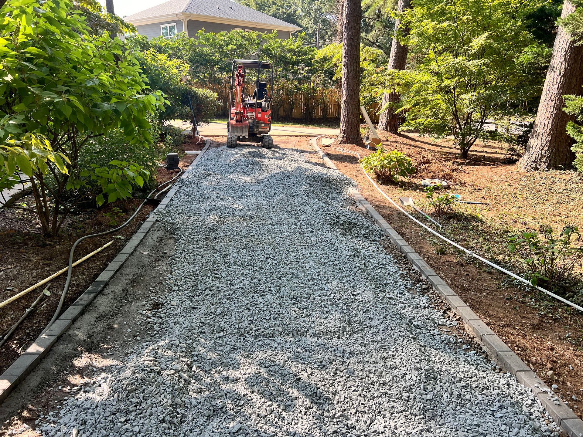 Gravel path under construction with a small red compactor in a leafy yard
