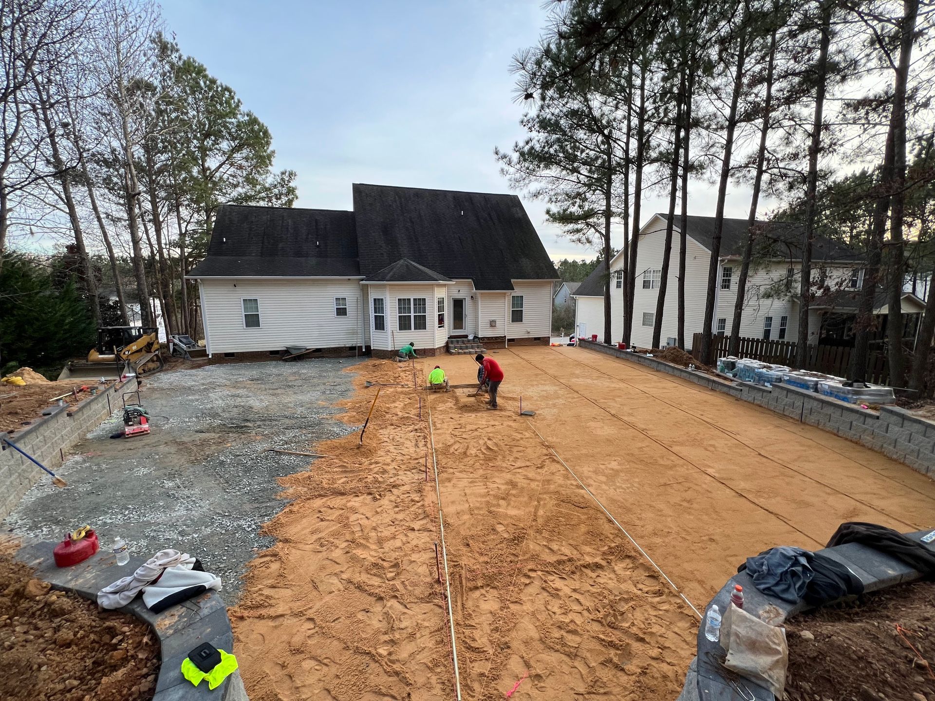 Construction site with workers leveling dirt in front of a house under renovation