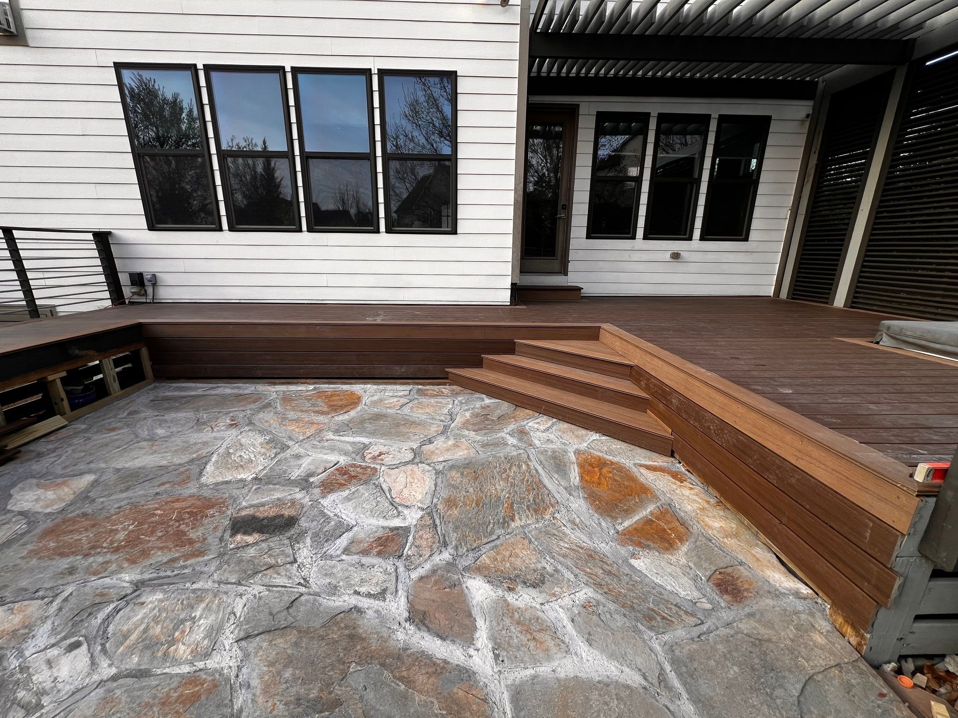 Stone patio with wooden steps and bench seating beside a house deck
