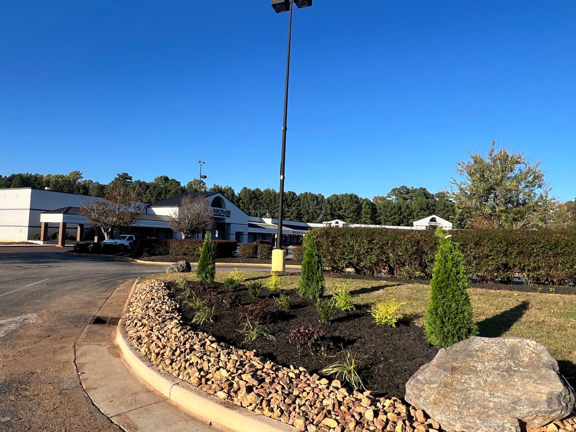Landscaped entrance with rock garden, shrubs, parking lot, and low building under a clear blue sky