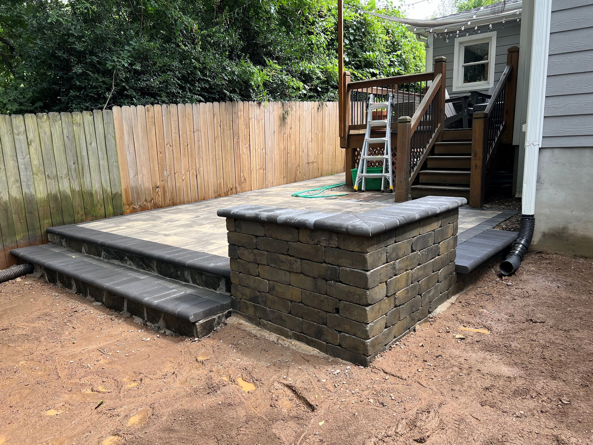 Backyard with raised wooden deck, steps, and brick retaining wall beside a dirt yard and fence