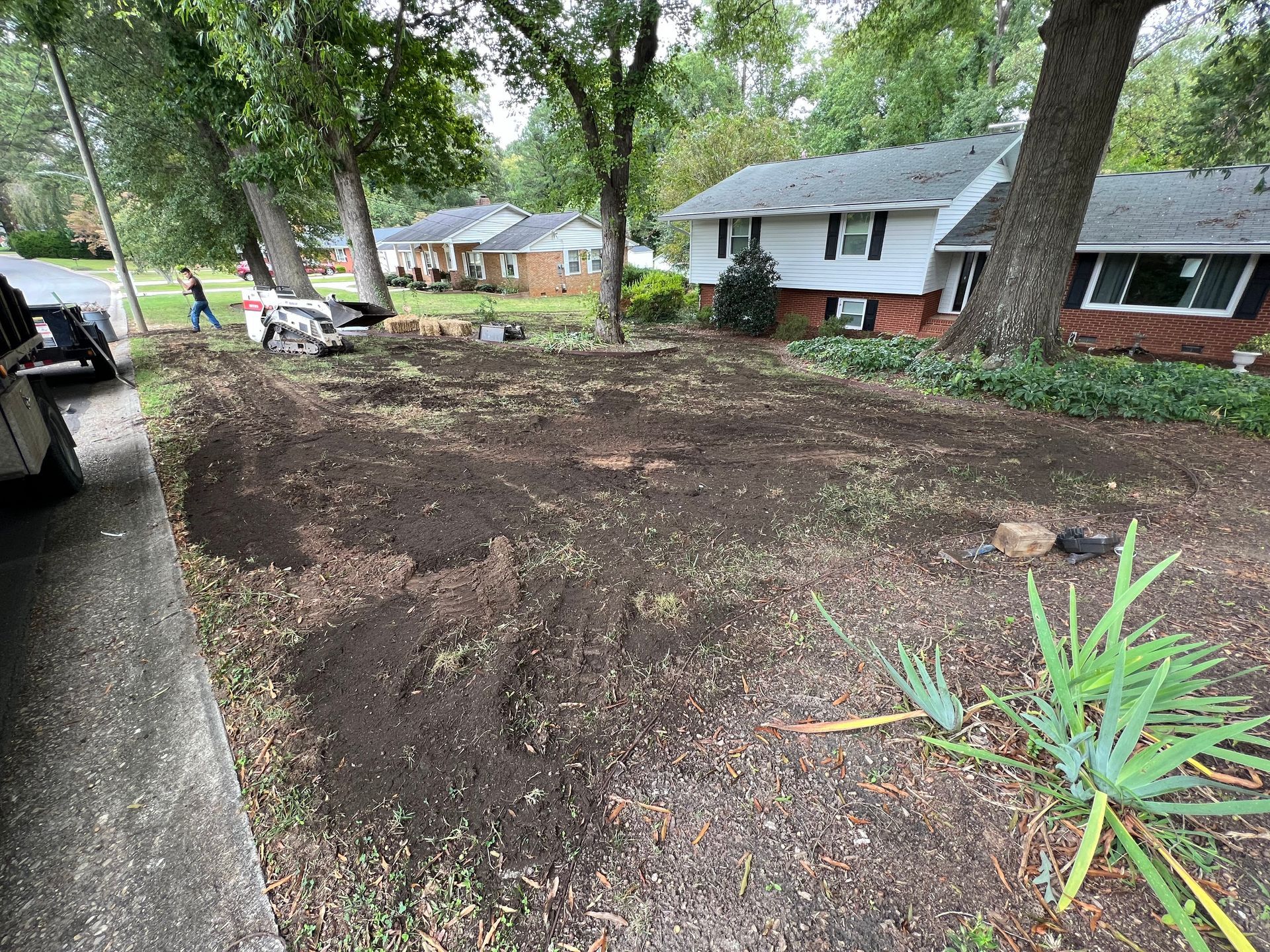Fresh mulch spread across a front yard beside a driveway, with trees and houses in the background.