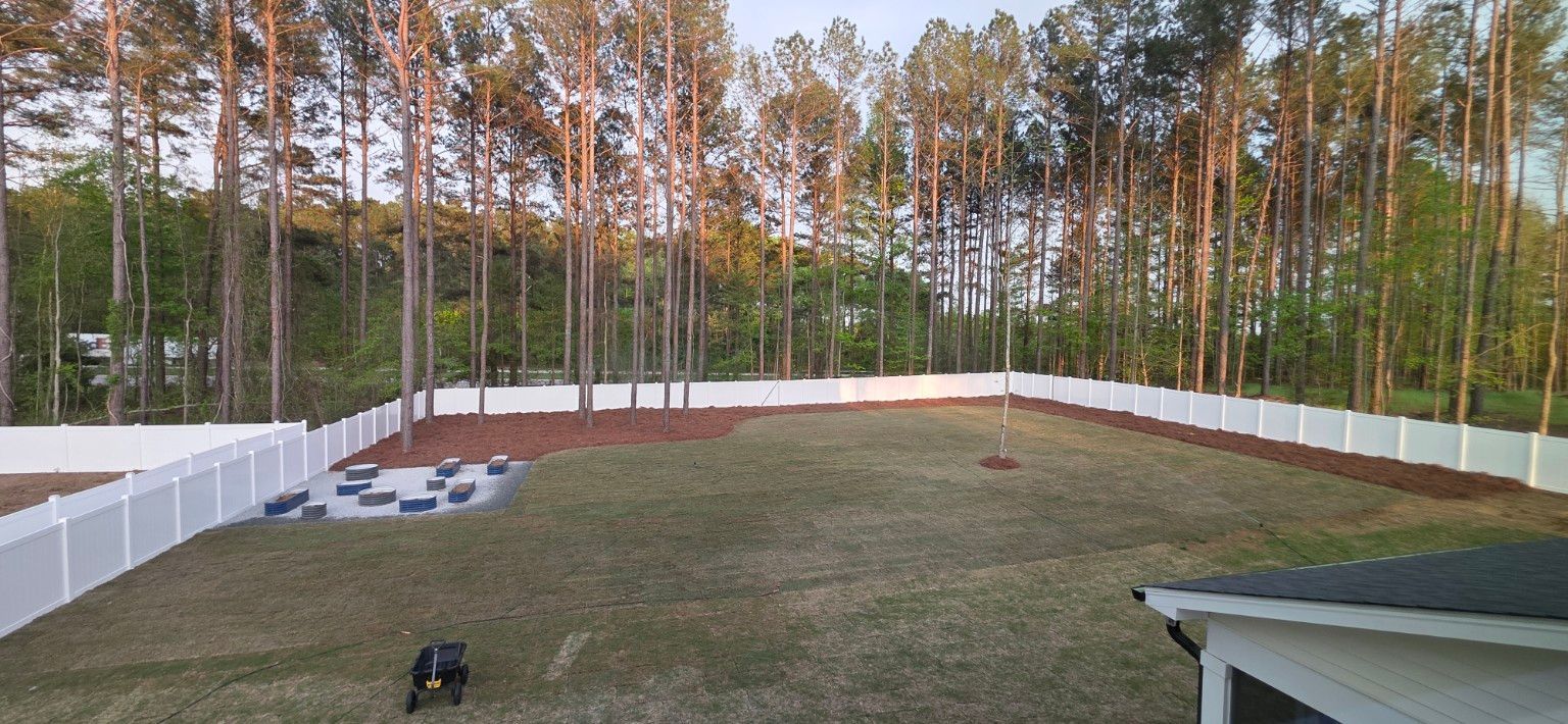 Backyard with a fenced-in grassy yard, tall trees, and a small deck in the corner.