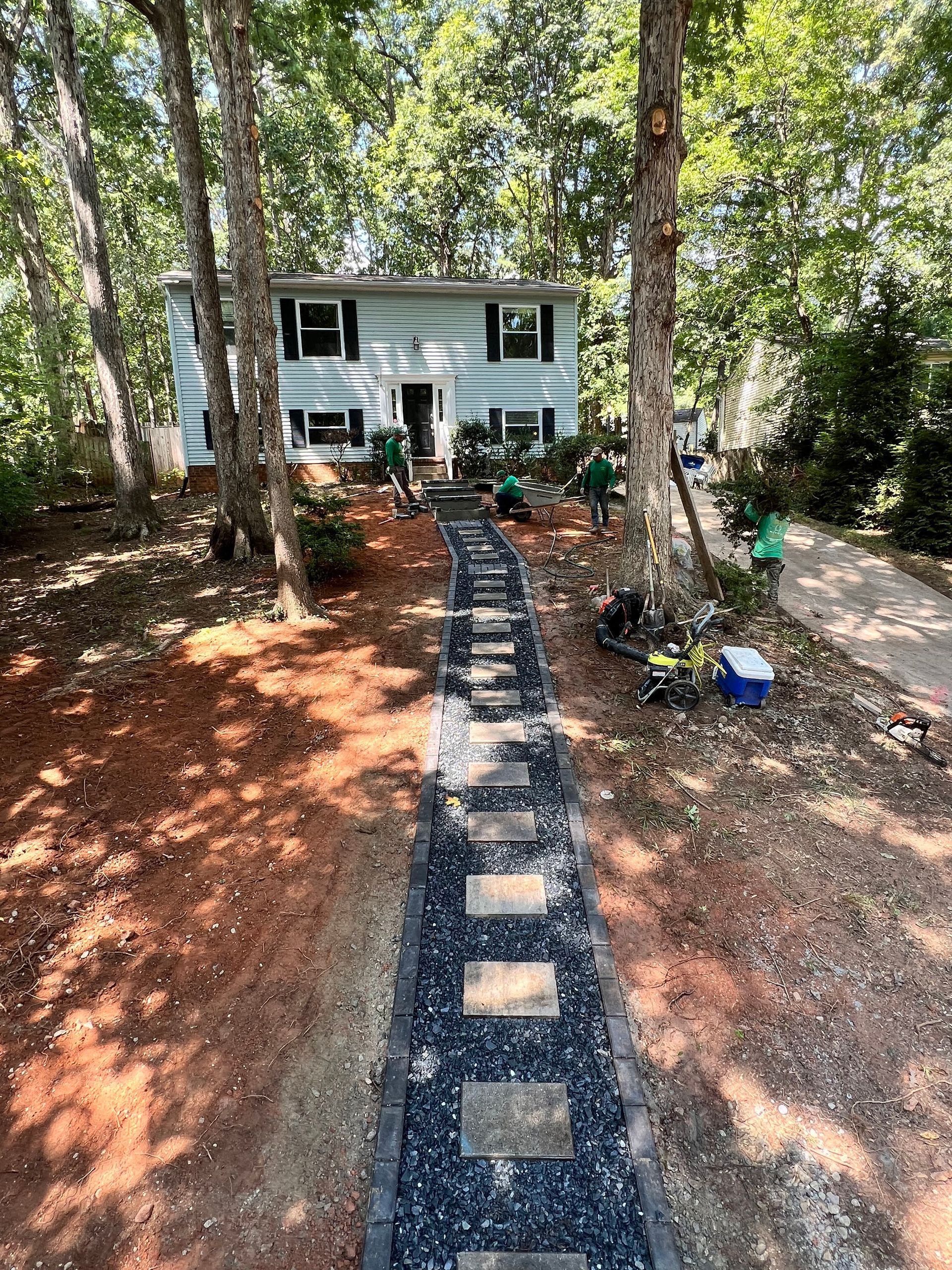 Front yard path of stepping stones leading to a white house amid trees and garden plants